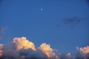 A moon and clouds in the sky with a blue sky